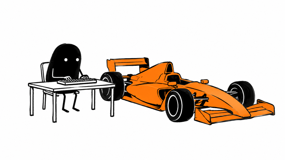 Lev types at a plain desk with a low racing car parked right beside it, nose pointing away.